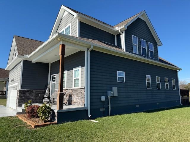 view of side of home featuring a garage, driveway, a lawn, stone siding, and a porch