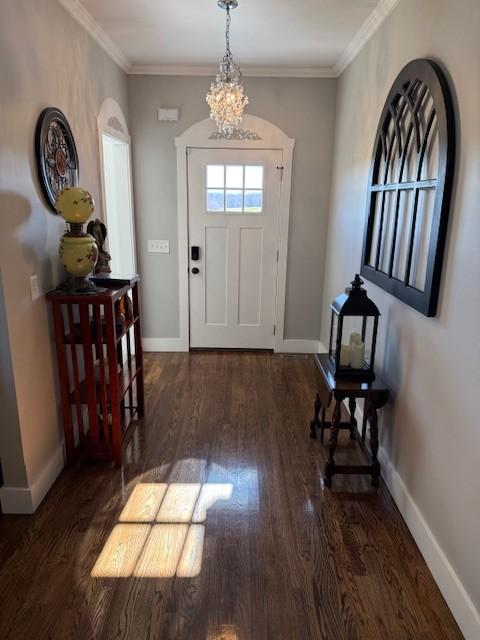 foyer with a notable chandelier, ornamental molding, wood finished floors, and baseboards