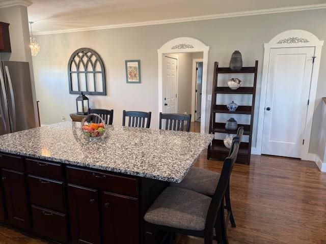 kitchen with light stone counters, a breakfast bar, dark wood finished floors, ornamental molding, and a kitchen island