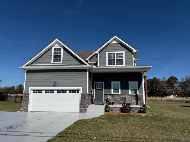 craftsman-style home with covered porch, driveway, and a front lawn