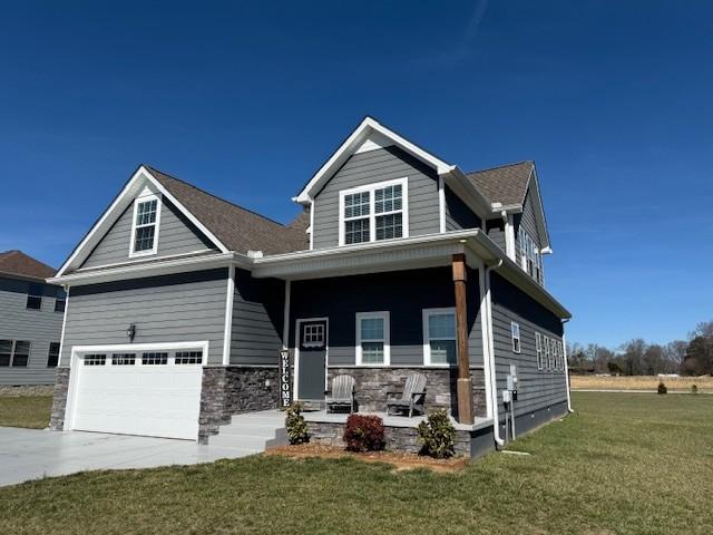 craftsman inspired home featuring stone siding, an attached garage, driveway, and a front lawn