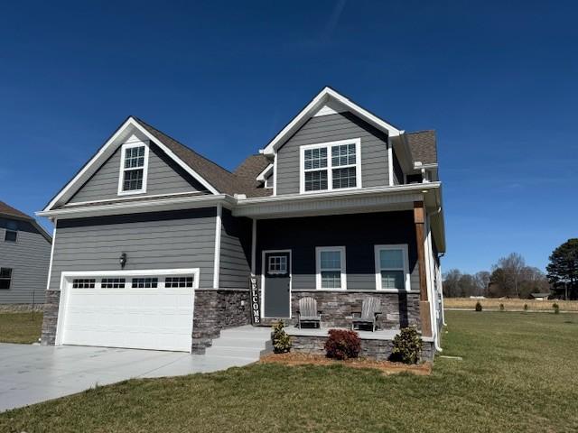 craftsman-style home featuring concrete driveway, stone siding, an attached garage, covered porch, and a front yard