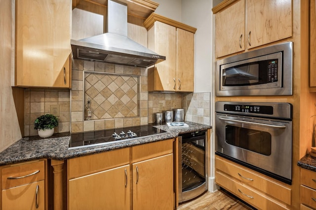 kitchen with stainless steel appliances, beverage cooler, wall chimney exhaust hood, and dark stone countertops