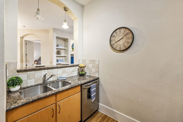 kitchen featuring backsplash, stainless steel dishwasher, sink, wood-type flooring, and hanging light fixtures