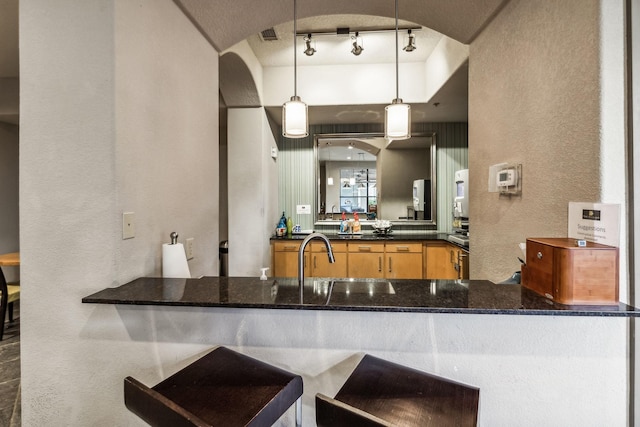 kitchen with sink, rail lighting, kitchen peninsula, dark stone countertops, and pendant lighting