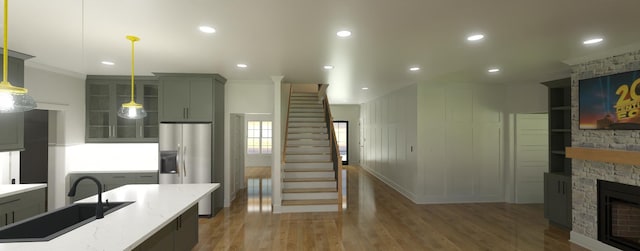 kitchen featuring sink, wood-type flooring, pendant lighting, stainless steel fridge with ice dispenser, and a stone fireplace