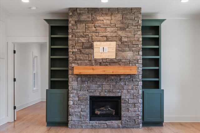 unfurnished living room with built in shelves, wood finished floors, baseboards, and a large fireplace