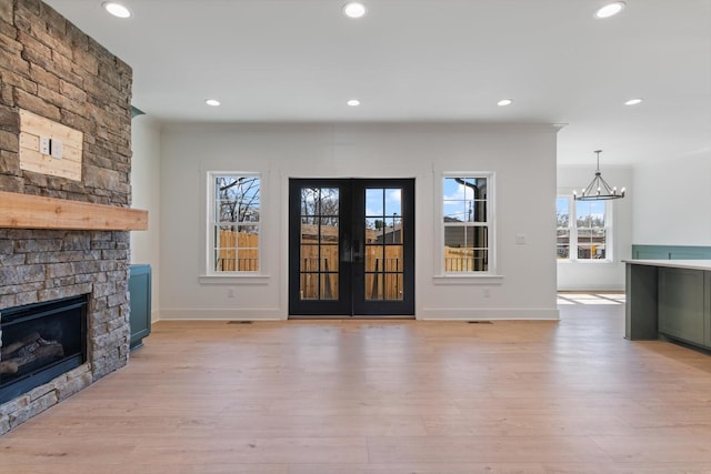 unfurnished living room featuring french doors, a stone fireplace, and light wood finished floors