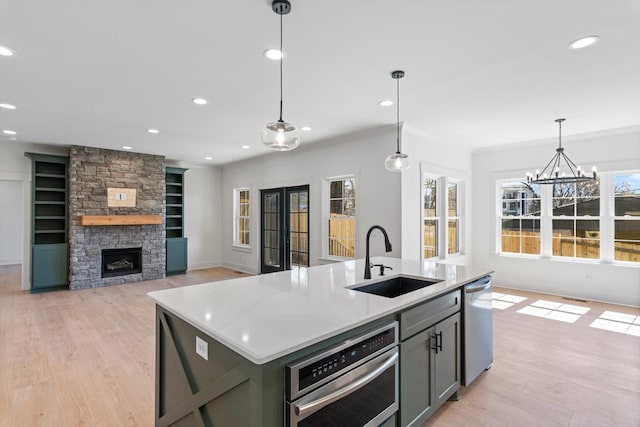 kitchen with light wood finished floors, a fireplace, a sink, french doors, and appliances with stainless steel finishes