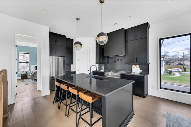 kitchen with sink, wall chimney range hood, a kitchen breakfast bar, a kitchen island with sink, and appliances with stainless steel finishes