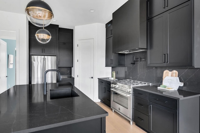 kitchen featuring appliances with stainless steel finishes, tasteful backsplash, sink, wall chimney range hood, and dark stone countertops