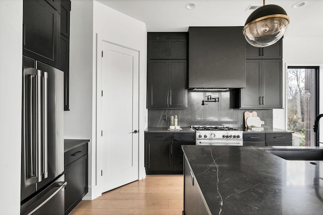 kitchen with decorative backsplash, extractor fan, high quality appliances, light hardwood / wood-style floors, and hanging light fixtures