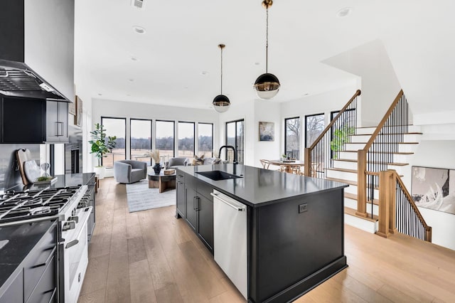 kitchen with dishwasher, wall chimney range hood, sink, high end stove, and decorative light fixtures