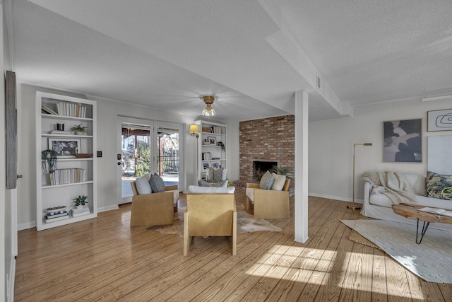 living room with light hardwood / wood-style floors, a brick fireplace, built in shelves, and a textured ceiling