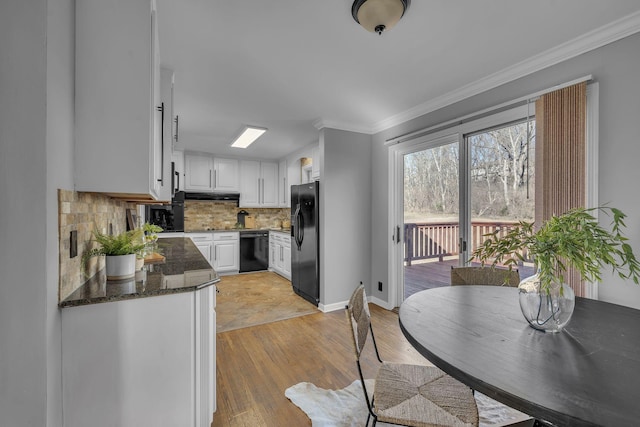 kitchen with black appliances, white cabinetry, decorative backsplash, light hardwood / wood-style flooring, and dark stone counters