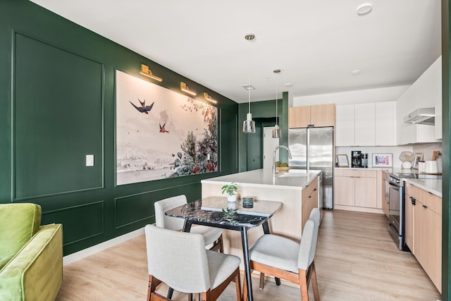 kitchen featuring a kitchen island with sink, black range with electric stovetop, stainless steel fridge, decorative light fixtures, and extractor fan