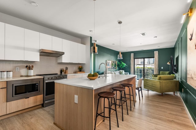 kitchen featuring white cabinetry, backsplash, an island with sink, decorative light fixtures, and appliances with stainless steel finishes