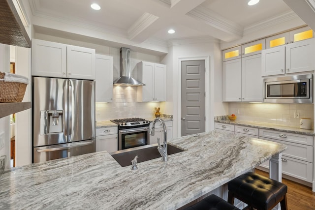 kitchen with wall chimney range hood, a breakfast bar, beam ceiling, stainless steel appliances, and white cabinets