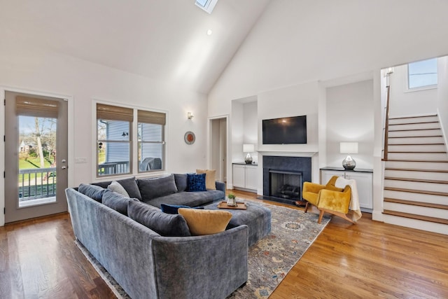 living room with a skylight, high vaulted ceiling, and light hardwood / wood-style flooring