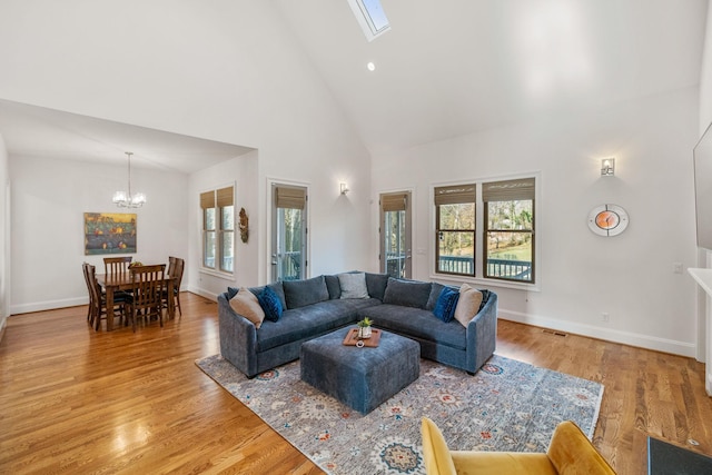 living room with light hardwood / wood-style flooring, an inviting chandelier, high vaulted ceiling, and a skylight