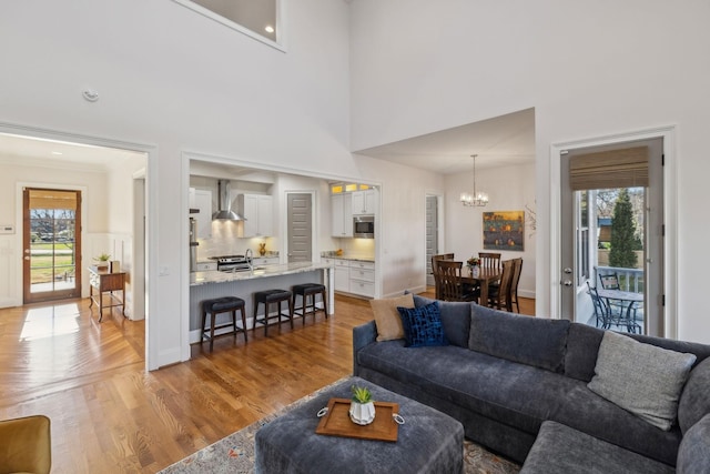 living room featuring a notable chandelier, a towering ceiling, light hardwood / wood-style flooring, and a healthy amount of sunlight