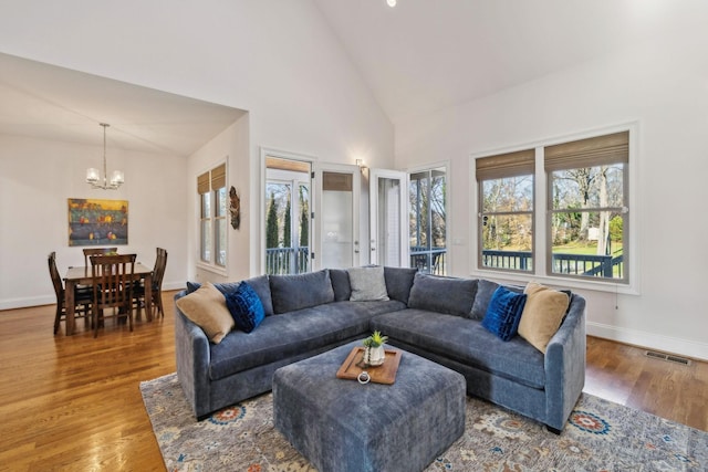 living room featuring wood-type flooring, a wealth of natural light, high vaulted ceiling, and a notable chandelier