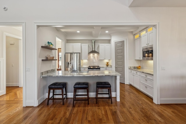 kitchen with white cabinets, backsplash, stainless steel appliances, light stone countertops, and wall chimney range hood