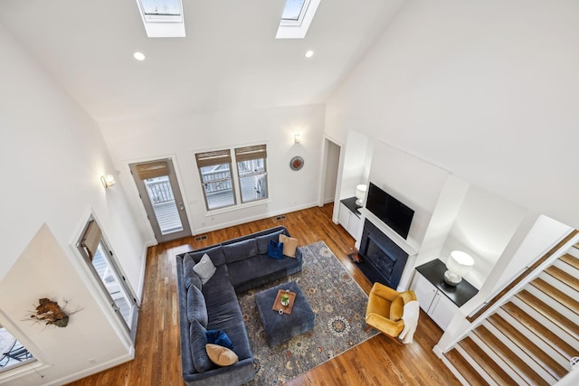 living room featuring hardwood / wood-style flooring, a skylight, and high vaulted ceiling