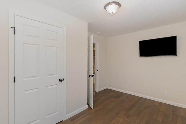 interior space featuring a textured ceiling, dark wood-style flooring, and baseboards