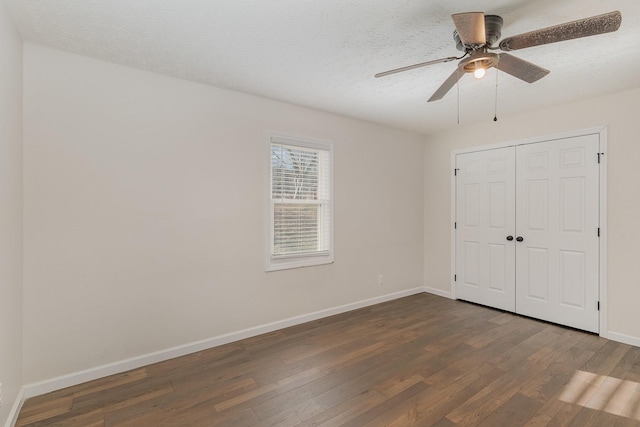 unfurnished bedroom featuring dark wood-type flooring, a closet, a textured ceiling, and baseboards