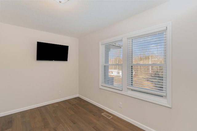 empty room featuring baseboards, visible vents, and dark wood-style flooring