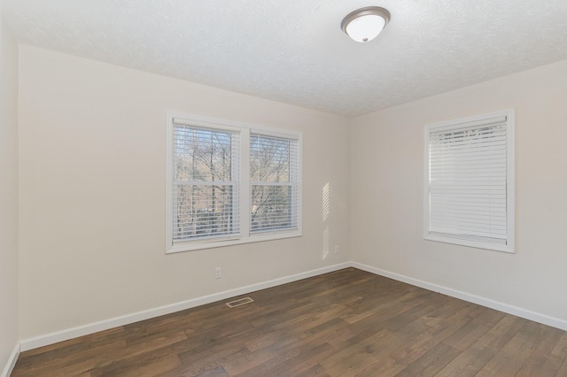 empty room with baseboards, a textured ceiling, visible vents, and dark wood-style flooring