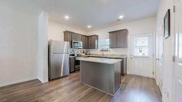 kitchen featuring appliances with stainless steel finishes, light stone counters, dark brown cabinets, a center island, and dark hardwood / wood-style floors