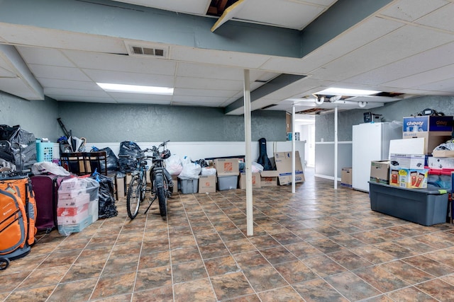 basement with a drop ceiling and white fridge