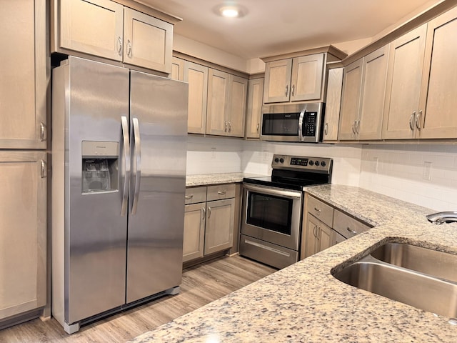 kitchen with light stone counters, sink, light wood-type flooring, and appliances with stainless steel finishes