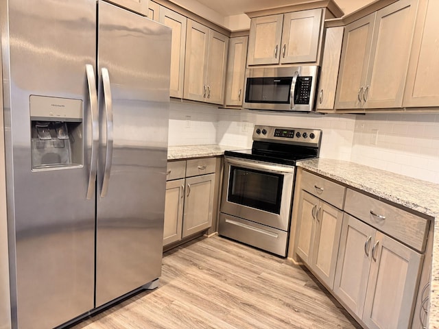 kitchen with backsplash, light stone counters, light hardwood / wood-style floors, and appliances with stainless steel finishes