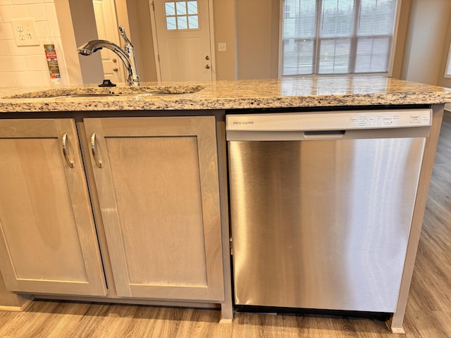 kitchen featuring light brown cabinets, sink, stainless steel dishwasher, light hardwood / wood-style floors, and light stone counters