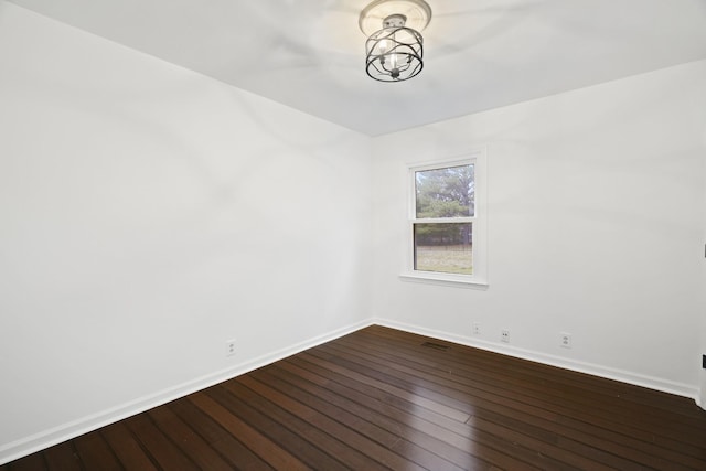 spare room with dark wood-style flooring, baseboards, and an inviting chandelier