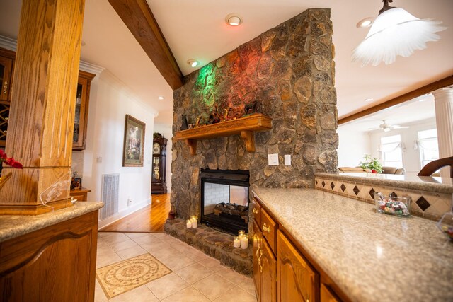 kitchen featuring ceiling fan, crown molding, light tile patterned floors, beam ceiling, and a fireplace