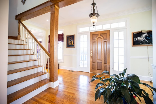 entryway with decorative columns, ornamental molding, and light wood-type flooring