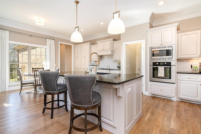 kitchen with backsplash, stainless steel appliances, a kitchen island with sink, pendant lighting, and white cabinets