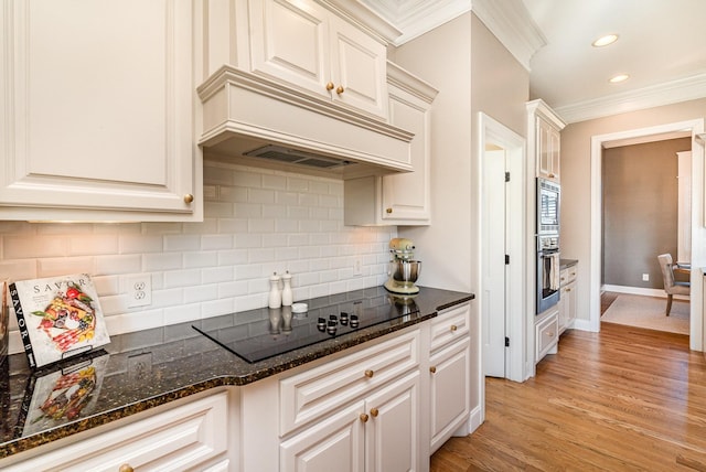 kitchen with white cabinets, crown molding, dark stone countertops, light wood-type flooring, and stainless steel appliances