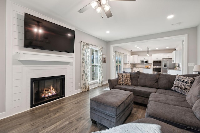 living room featuring a fireplace, ceiling fan, and dark wood-type flooring