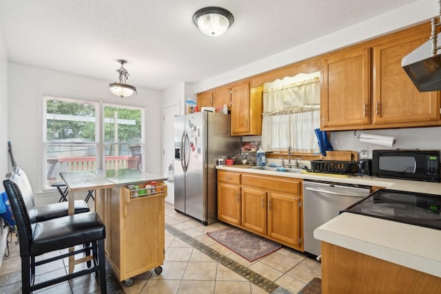 kitchen with appliances with stainless steel finishes, sink, light tile patterned floors, pendant lighting, and a center island