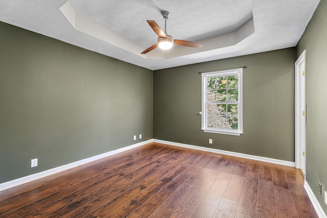 spare room with a tray ceiling, ceiling fan, dark wood-type flooring, and a textured ceiling