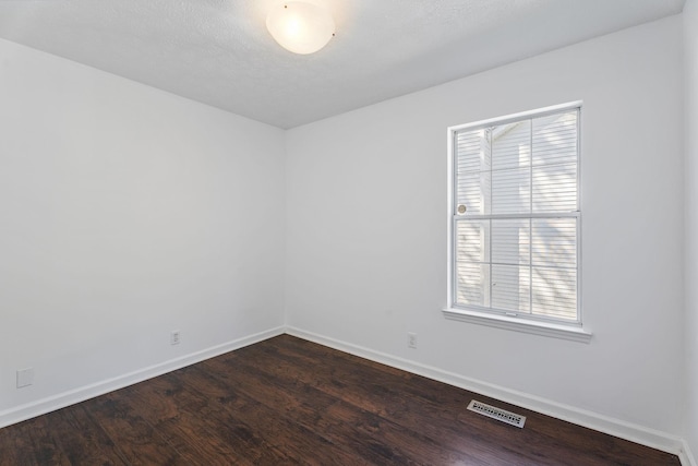 empty room with a wealth of natural light and dark hardwood / wood-style floors