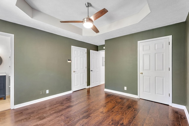 unfurnished bedroom with connected bathroom, a raised ceiling, ceiling fan, and dark wood-type flooring