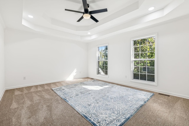 carpeted empty room with a raised ceiling and ceiling fan