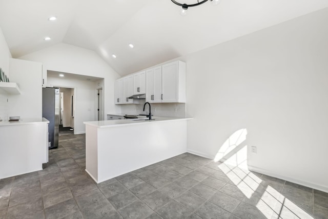 kitchen featuring kitchen peninsula, stainless steel fridge, vaulted ceiling, sink, and white cabinets