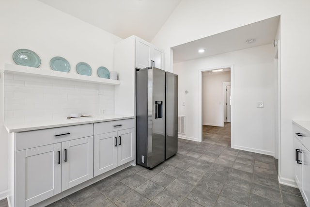 kitchen with decorative backsplash, stainless steel fridge, white cabinetry, and vaulted ceiling